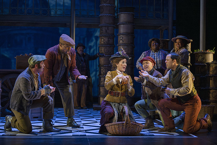 Kristi Frank as Eliza Doolittle with (l to r) Gryphyn Karimloo, Allan Louis, Graeme Kitagawa, JJ Gerber and members of the cast. (Shaw Festival, 2024). Photo by David Cooper.